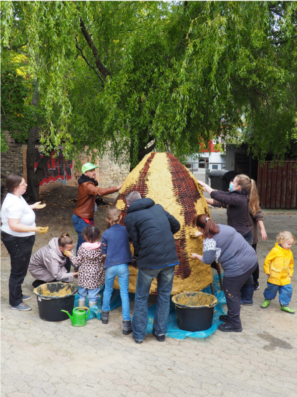 Kinder und Eltern beim Bau einer Lehmhütte